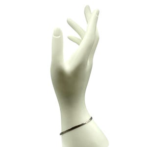 Puede incluir: Una pulsera de cadena de espiga fina y metálica con un acabado plateado pulido. La pulsera presenta un diseño de eslabones planos y flexibles que se envuelve alrededor de la muñeca, mostrando una superficie lisa y reflectante.