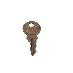 May include: A brass-coloured metal key with a circular head featuring the embossed text American U.S.A. The key has a central vertical groove and a jagged, irregular blade profile designed for a specific lock mechanism, showing signs of age.