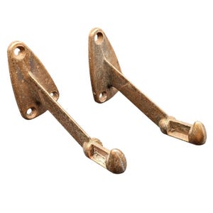 May include: Two matching wall-mounted hooks with a weathered bronze finish. Each hook features a triangular mounting plate with two circular screw holes and a long, straight arm extending outward, ending in a curved, upward-facing hook tip.