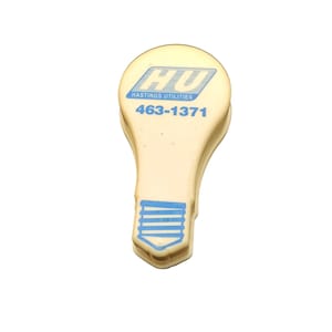 May include: A light beige, lightbulb-shaped clip with blue text and graphics. The text reads "HU" above "HASTINGS UTILITIES" and the phone number "463-1371". The bottom of the clip has a blue lightbulb design.