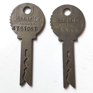 May include: Two vintage metal keys with the text "BELL LOCK" and "PATENTED" above the number "47S1087". The keys have a circular top with a hole and a serrated edge. The key shafts have a unique wavy design.
