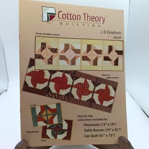 May include: A quilting pattern booklet for 3-D Pinwheels, featuring a red, white, and brown color scheme. The booklet includes instructions for making placemats, a table runner, and a lap quilt. The pattern is #QY37.