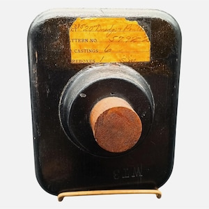May include: A dark brown, rectangular bottle with a cork stopper. A yellowed label with handwritten text is affixed to the bottle. The bottle is displayed on a gold-colored metal stand. The text on the label reads "39520 Davidson Point".
