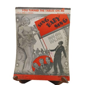 May include: Vintage sheet music cover for "Sing Baby Sing" featuring a woman in a ruffled costume and a man in a suit. The cover is predominantly gray, red, and white, with text including the song title and lyrics.