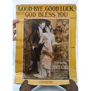 Puede incluir: Una portada de partitura musical vintage con fondo amarillo y una ilustración en blanco y negro de una pareja de pie en un jardín. El título de la canción es "Good-Bye, Good Luck, God Bless You" y la canción es una balada. Los compositores son J. Keirn Brennan y Ernest R. Ball.