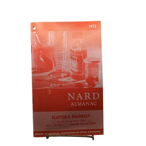 Könnte beinhalten: Ein NARD Almanac Heft aus dem Jahr 1972 von Clayton's Pharmacy in Grand Island, Nebraska. Das Cover zeigt eine einfarbige orangefarbene Grafik mit Apothekengeräten, darunter ein Messzylinder, eine Glasflasche und ein Löffel auf einem Tisch.