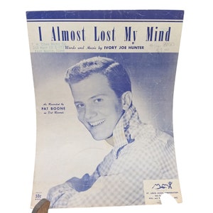 Puede incluir: Una portada de partitura vintage con un joven sonriente que lleva una camisa a cuadros azules y blancos. El título de la canción es "I Almost Lost My Mind" y la música se atribuye a Ivory Joe Hunter. La partitura tiene un precio de 50 centavos.