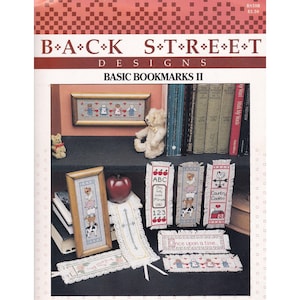 May include: A book cover titled "BACK STREET DESIGNS BASIC BOOKMARKS II" with various cross-stitch bookmark designs. The bookmarks feature images of farm animals, children, and the text "ABC". There is also a small teddy bear.