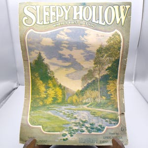 Op de afbeelding: Vintage bladmuziekcover voor "Sleepy Hollow" met een landschapsillustratie. Het kunstwerk toont een rivierlandschap met bomen, een huis en waterlelies. De titel en de tekst "Where I First Met You" staan bovenaan.