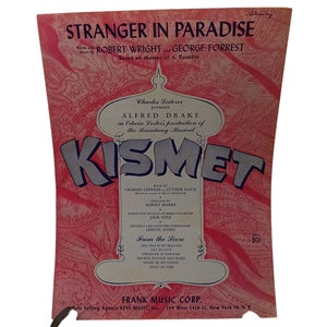 Op de afbeelding: Een roze en witte bladmuziekhoes voor de musical "Kismet" met het nummer "Stranger in Paradise". De hoes heeft een grote, gestileerde afbeelding van een moskee met de titel van de musical in grote, vetgedrukte letters.