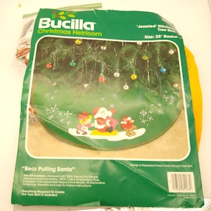Könnte beinhalten: Ein Bucilla Christmas Heirloom Baumrock-Kit mit einer grünen Filzbasis und einem festlichen Design. Das Kit enthält Stempelfilz, Stickgarn, Pailletten und Perlen. Das Design ist 89 cm rund und zeigt den Weihnachtsmann, der von einem Bären gezogen wird.