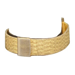 Puede incluir: Una pulsera de reloj de metal dorado con un patr&oacute;n texturizado. La pulsera tiene un cierre de hebilla.