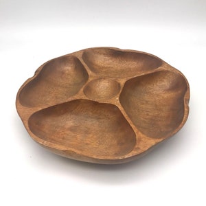 May include: A round wooden serving tray with five separate compartments. The tray is made of dark brown wood and has a natural, rustic finish.