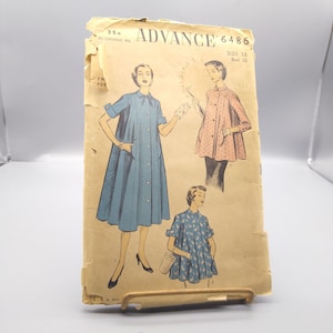 Pode incluir: Modelo de costura vintage para um vestido, Advance 6486, tamanho 12, busto 30. O modelo mostra um vestido azul com mangas curtas e fecho de botões na frente, um vestido rosa com mangas curtas e fecho de botões na frente, e um vestido estampado azul e branco com mangas curtas e fecho de botões na frente.