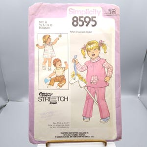 May include: A vintage Simplicity sewing pattern for toddler clothing, size H (1/2, 1, and 2). The pattern features illustrations of children wearing the outfits. The pattern includes the text "Time Saver Stretch Knit".