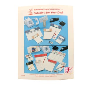 May include: A craft instruction leaflet titled BumbleBee Enterprises presents Stitchin's for Your Desk, featuring charted designs for lucite note pads, loose leaf pads, letter holders, stamp dispensers, calendar pads, and clips with various colorful patterns.