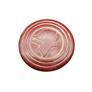 May include: A red plastic round button with a raised design of a woman's profile with a hat and flowing hair.