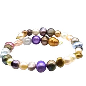 May include: A multi-colored pearl bracelet featuring a variety of shapes and hues. The pearls range in color from white, pink, and gold to purple, green, and gray. The bracelet is strung together with a delicate gold-colored wire.