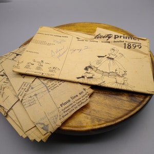 Puede incluir: Patrón de costura vintage para un vestido con ribete de encaje. El patrón se titula "licity prime" y el año es 1899. El patrón está sobre una superficie de madera.