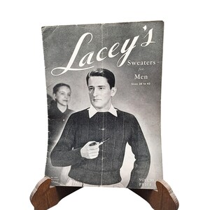 May include: Vintage black and white magazine cover for "Lacey's Sweaters for Men." The cover features a man in a dark sweater with a white collar, holding a pipe. The magazine is propped up on a wooden stand.