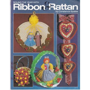 May include: A vintage craft book cover titled "Round the Year with Ribbon & Rattan" by Constance Spates. The cover features handmade rattan and ribbon crafts, including a wreath with dolls, heart-shaped decorations, and a basket with flowers.