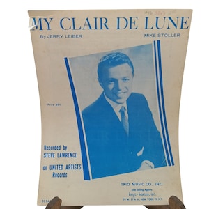 Puede incluir: Una portada de partitura vintage para la canción "My Clair De Lune" de Jerry Leiber y Mike Stoller. La portada presenta una foto en blanco y negro de Steve Lawrence, quien grabó la canción en United Artists Records. La partitura tiene un precio de 60 centavos y es publicada por Trio Music Co., Inc.