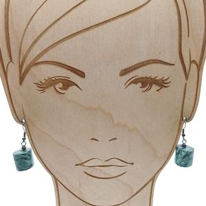 May include: A pair of earrings with a silver hook and a square, green marbled stone. The earrings are displayed on a wooden face-shaped jewelry holder. The earrings are a simple, elegant design.
