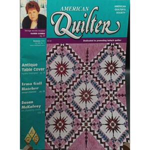 May include: The cover of the "American Quilter" magazine, Summer 2003 issue, features a quilt pattern with starburst designs in shades of red, white, and purple. The magazine's title is in a teal font, and the cover includes articles on antique table covers and design checklists.