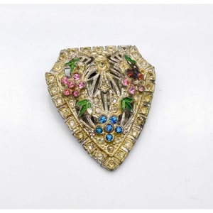 May include: A vintage gold-toned brooch with a triangular shape. The brooch is decorated with a floral design featuring pink, blue, and green enamel. The center of the brooch has a clear rhinestone.