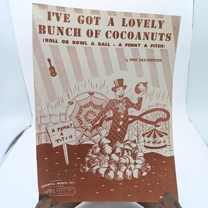 May include: A vintage sheet music cover with a brown and white striped background. The title is "I've Got A Lovely Bunch Of Cocoanuts (Roll Or Bowl A Ball - A Penny A Pitch)" by Fred Heatherton. The illustration shows a clown with a red and white costume holding a coconut and standing on a pile of coconuts. There is a carnival scene in the background.