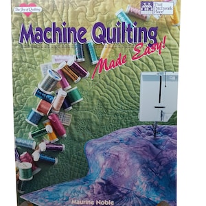 Puede incluir: Un libro titulado "Machine Quilting Made Easy!" de Maurine Noble. La portada presenta una colcha colorida, carretes de hilo y una máquina de coser.