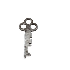 Könnte beinhalten: Ein silberfarbener Skelettschlüssel mit einem kleeblattartigen Kopf. Der Schlüssel ist mit "Yale Lock Co.  New York, U.S.A." gekennzeichnet.