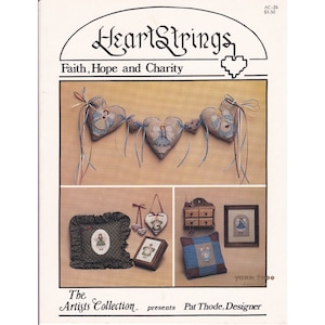 May include: A cross stitch pattern booklet titled "HeartStrings: Faith, Hope and Charity" by The Artists Collection, featuring a design of a garland of angels with hearts and a variety of other cross stitch designs.