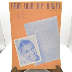 Puede incluir: Una portada de partitura vintage para la canción "Tears From My Inkwell" con una foto de George Olsen y su orquesta. La portada es de color melocotón con texto azul y una nota manuscrita en una hoja de papel azul.