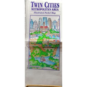 以下が含まれることがあります： ツインシティーズ都市圏のイラスト入りポケットマップ。この地図は、街のスカイライン、橋、蒸気船のある川をカラフルに描いています。「ツインシティーズ」というタイトルは、大きな紫色の文字で書かれています。