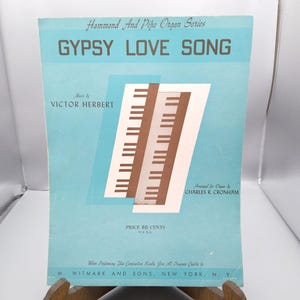 Puede incluir: Partitura vintage titulada "Gypsy Love Song" de la serie Hammond And Pipe Organ. La portada es azul claro con el título en letras azul oscuro. Presenta una ilustración de teclado de piano y el nombre del compositor, Victor Herbert.