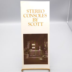 May include: A brochure advertising stereo consoles by Scott. The brochure features a photo of a dark wood stereo console with glass doors in a dimly lit room.