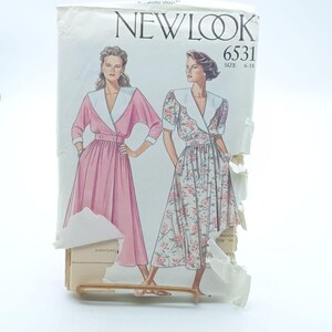 Könnte beinhalten: Ein Vintage New Look Schnittmuster mit Illustrationen von zwei Kleidern. Eines ist einfarbig rosa mit weißem Kragen, das andere floral mit weißem Kragen. Die Schnittmusternummer ist 6531, Größen 6-18.