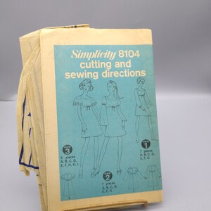 May include: Vintage Simplicity sewing pattern 8104 for a dress with three different views. The pattern is printed on a light blue background with black lines and text. The text includes "Simplicity 8104", "cutting and sewing directions", "view 1", "view 2", and "view 3".