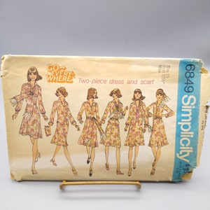 May include: Simplicity sewing pattern number 6849 for a two-piece dress and scarf. The pattern is for size 10, bust 32 1/2 inches. The pattern shows a woman wearing a floral print dress with a matching scarf. The text "GO EVERYWHERE" is printed on the pattern.
