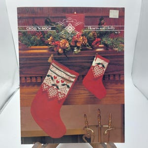May include: Cross stitch pattern for a Christmas stocking with the text "Merry Christmas" and a heart design. The pattern is titled "Hearts and Holly" and is number 73.