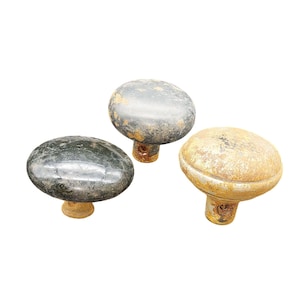 May include: Three antique cabinet knobs with a weathered appearance. The knobs have a rounded, oval shape and are in shades of gray, black, and gold. The knobs are made of metal and have a rustic, aged look.