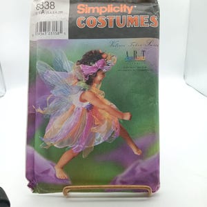 May include: Simplicity pattern number 8338 for a fairy costume. The pattern features a young girl wearing a colourful fairy costume with wings and a flower crown. The pattern is for sizes 3-8.