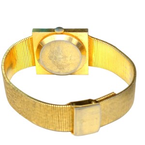 Puede incluir: Un reloj de pulsera dorado con una esfera cuadrada y una correa de malla dorada.