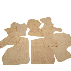 May include: A collection of vintage paper cutouts featuring red line drawings of various animals and figures. The cutouts include a cat, bunny, bear, duck, and a figure in pajamas. The paper has a cream color.
