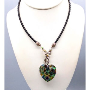 May include: A black leather cord necklace with a silver heart pendant. The heart is made of iridescent abalone shell with a green, blue, and gold pattern.