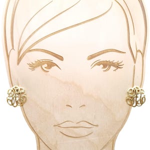 Puede incluir: Pendientes de monograma de oro con un diseño delicado e intrincado. Los pendientes se muestran en una cabeza de maniquí de madera.