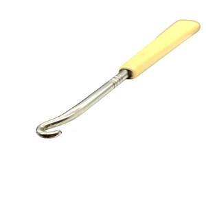 Könnte beinhalten: Ein Knopfhaken-Werkzeug mit einem polierten, silberfarbenen Metallschaft, der an einem Ende einen gebogenen Haken aufweist, und einem glatten, cremefarbenen Griff. Der Metallschaft ist mit drei feinen, horizontal eingravierten Ringen am Griff befestigt.