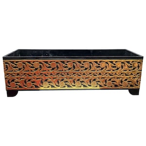 Pode incluir: Um recipiente retangular preto com um design de filigrana floral dourada. O recipiente tem um interior preto e assenta em quatro pequenos pés pretos. O design dourado é intrincado e envolve os lados.