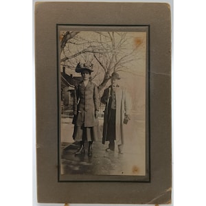 Fotografía vintage en blanco y negro de un hombre y una mujer con abrigos de invierno sobre un marco de cartón.